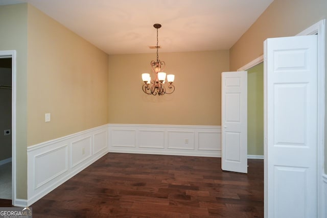 unfurnished dining area featuring a wainscoted wall, a chandelier, dark wood finished floors, and a decorative wall