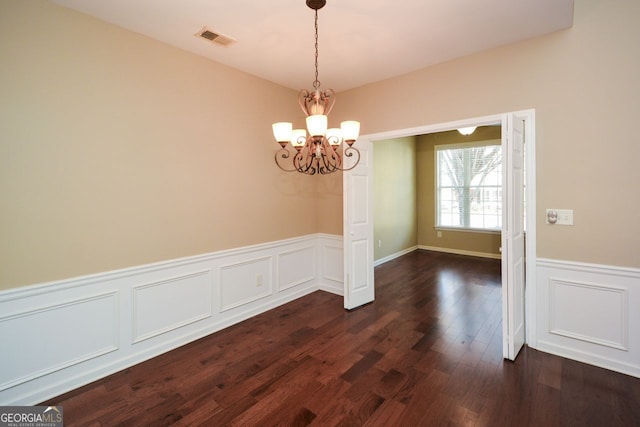 unfurnished dining area featuring dark wood finished floors, visible vents, wainscoting, and an inviting chandelier