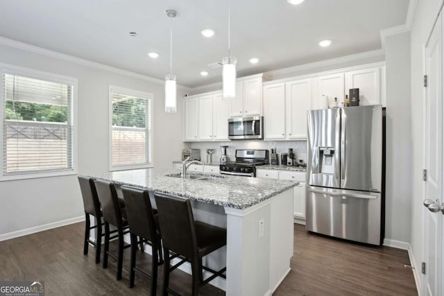 kitchen with light stone counters, stainless steel appliances, white cabinetry, and an island with sink