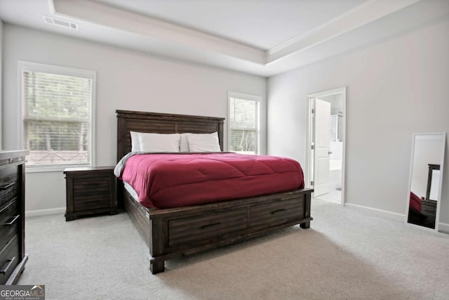 bedroom with connected bathroom, light colored carpet, and a tray ceiling