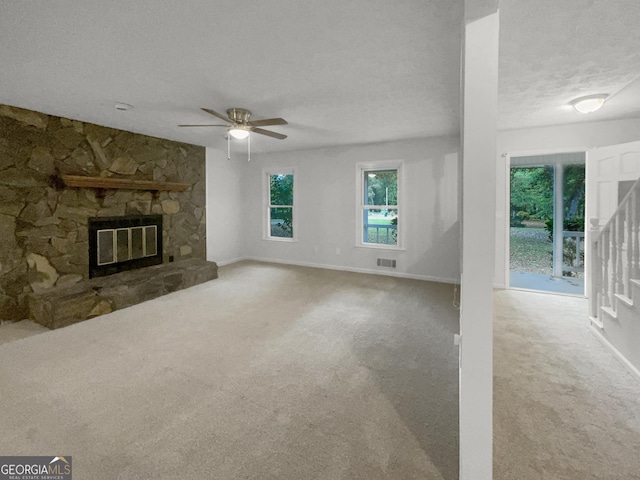 unfurnished living room featuring a textured ceiling, light colored carpet, a stone fireplace, and ceiling fan