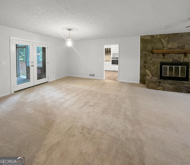 unfurnished living room featuring french doors, a textured ceiling, light colored carpet, and a stone fireplace