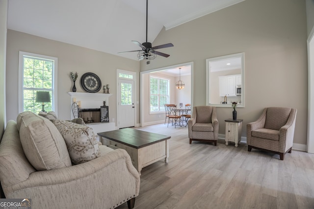 living room with ceiling fan with notable chandelier, light wood-type flooring, high vaulted ceiling, and a wealth of natural light