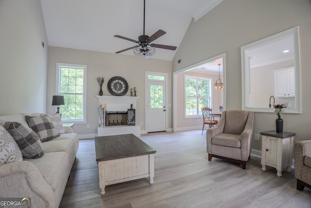 living room featuring ceiling fan with notable chandelier, a healthy amount of sunlight, light hardwood / wood-style floors, and high vaulted ceiling