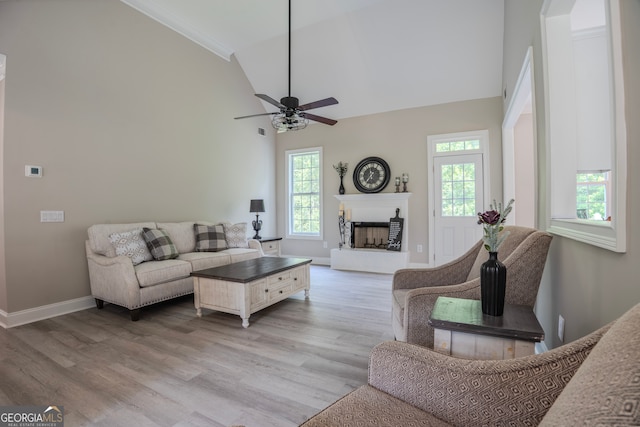 living room featuring ceiling fan, light wood-type flooring, crown molding, and high vaulted ceiling