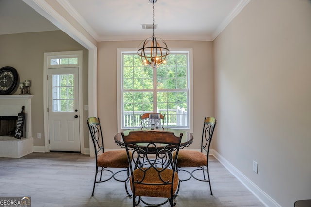 dining area with a fireplace, light hardwood / wood-style floors, an inviting chandelier, and ornamental molding