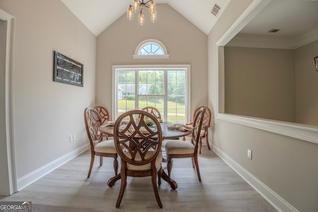 dining room with light wood-type flooring, high vaulted ceiling, an inviting chandelier, and crown molding