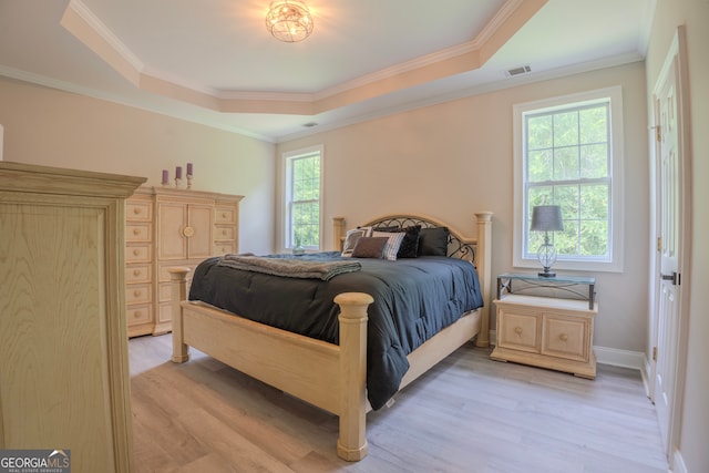 bedroom with a raised ceiling, crown molding, and light wood-type flooring