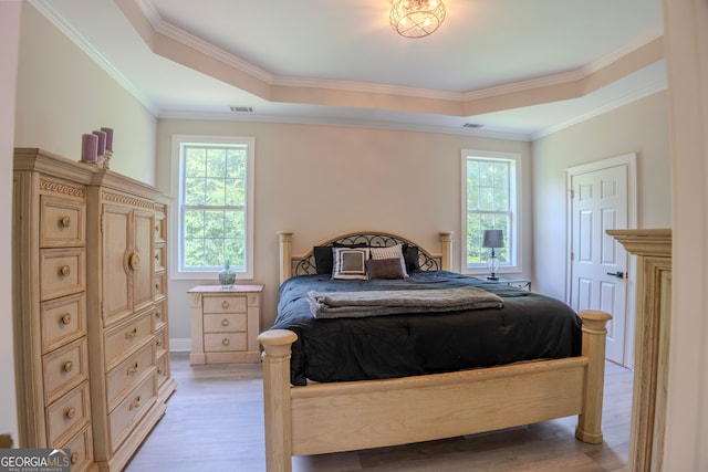 bedroom with light hardwood / wood-style floors, a raised ceiling, and crown molding