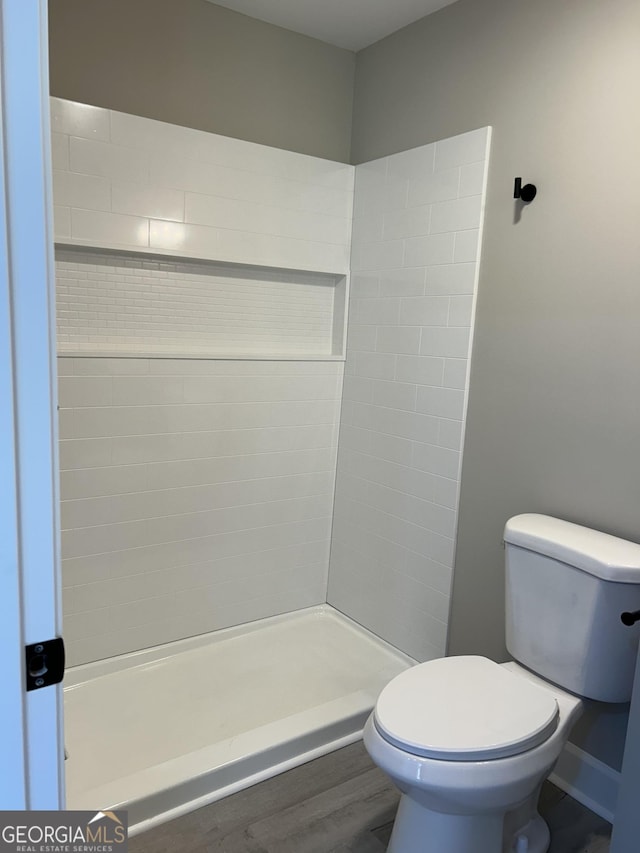 bathroom featuring hardwood / wood-style floors, toilet, and a tile shower