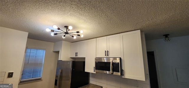 kitchen with tile patterned flooring, an inviting chandelier, white cabinets, and appliances with stainless steel finishes