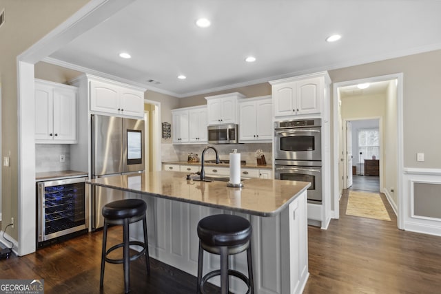 kitchen featuring a breakfast bar area, a center island with sink, stainless steel appliances, beverage cooler, and white cabinets