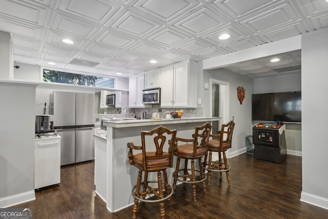 kitchen with white cabinetry, stainless steel appliances, tasteful backsplash, a kitchen bar, and kitchen peninsula