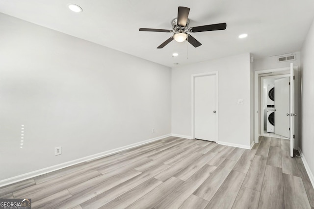 unfurnished bedroom featuring baseboards, light wood-type flooring, visible vents, and stacked washer / drying machine