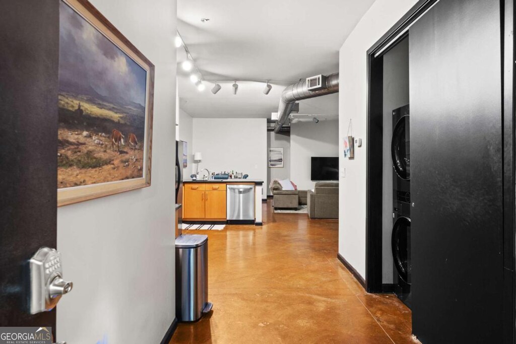 hall featuring rail lighting and stacked washer / drying machine