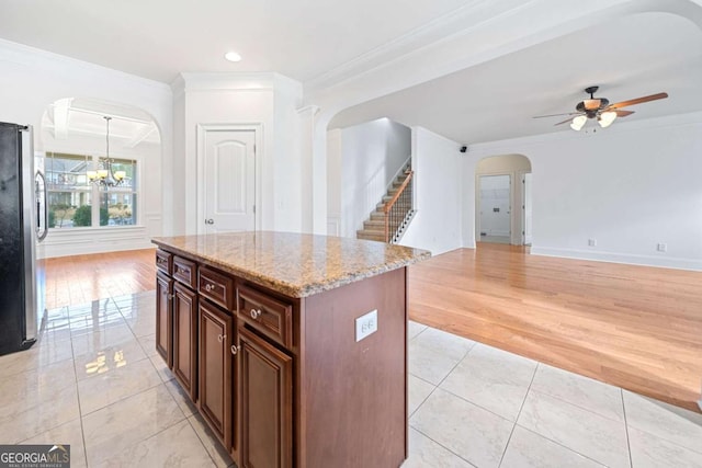 kitchen with stainless steel refrigerator, crown molding, light hardwood / wood-style floors, a kitchen island, and ceiling fan with notable chandelier