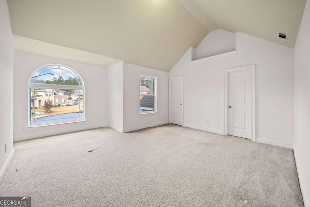 additional living space with light colored carpet, a healthy amount of sunlight, and high vaulted ceiling