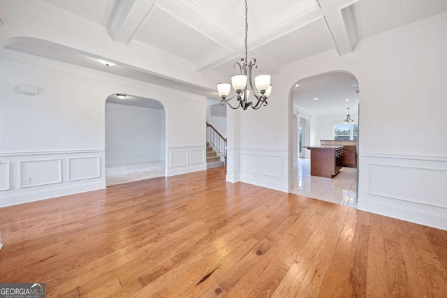 unfurnished dining area featuring a chandelier, beam ceiling, light wood-type flooring, and ornamental molding