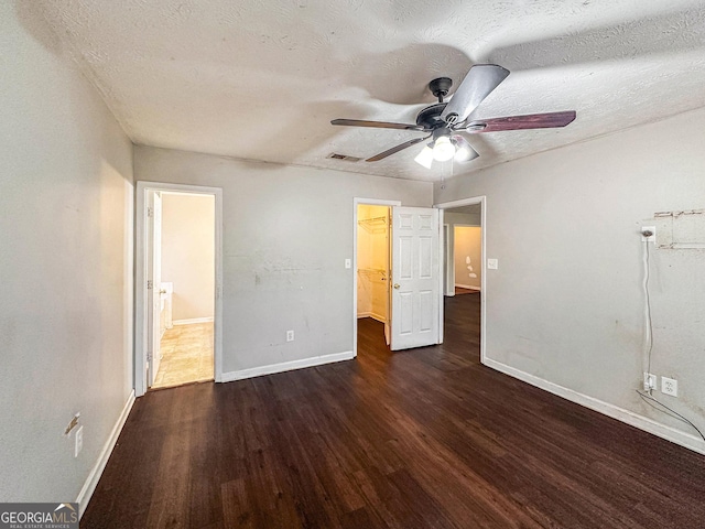 unfurnished bedroom featuring a walk in closet, a textured ceiling, ceiling fan, and dark wood-type flooring