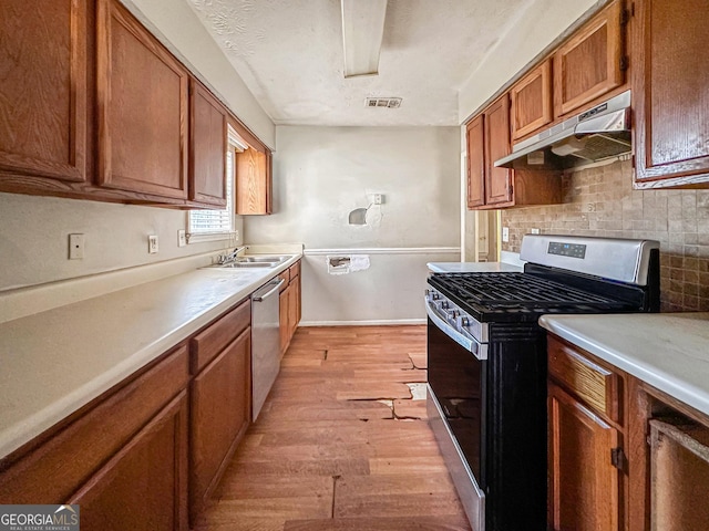 kitchen with exhaust hood, sink, appliances with stainless steel finishes, tasteful backsplash, and light hardwood / wood-style floors