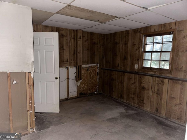 basement with a drop ceiling and wooden walls