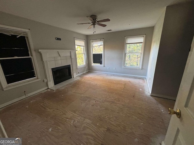 unfurnished living room with a tile fireplace, a wealth of natural light, and ceiling fan