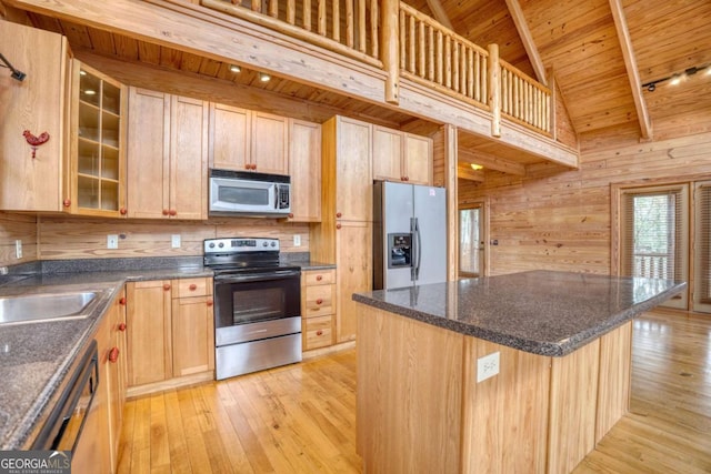 kitchen featuring appliances with stainless steel finishes, light hardwood / wood-style flooring, a kitchen island, and wooden walls