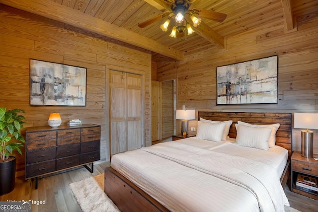 bedroom with beam ceiling, ceiling fan, wood walls, and light wood-type flooring