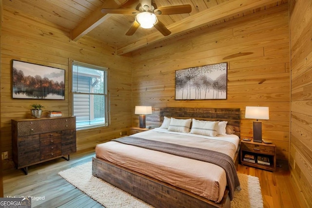 bedroom with ceiling fan, light hardwood / wood-style flooring, beamed ceiling, and wood walls