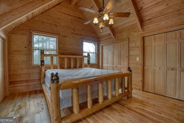 bedroom with vaulted ceiling with beams, wood walls, and light hardwood / wood-style flooring