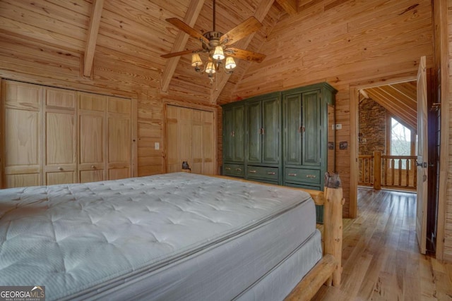 unfurnished bedroom featuring ceiling fan, wooden walls, wooden ceiling, vaulted ceiling with beams, and light hardwood / wood-style floors