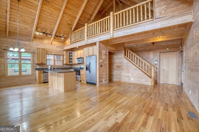 kitchen with wood walls, a center island, high vaulted ceiling, and appliances with stainless steel finishes