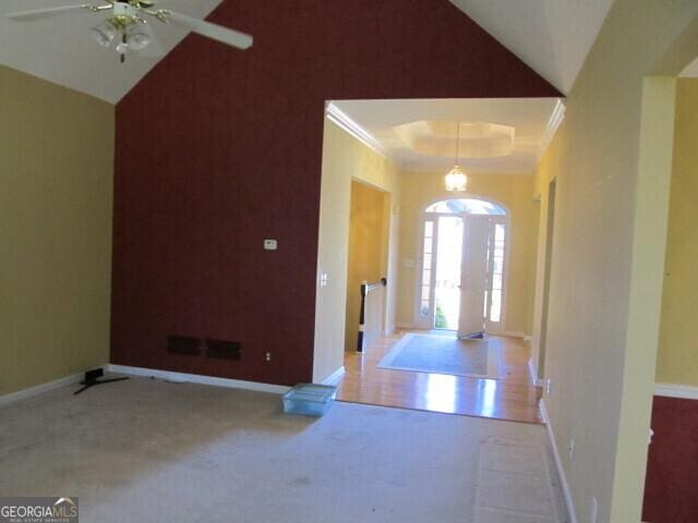 entryway featuring crown molding, ceiling fan, light carpet, and vaulted ceiling