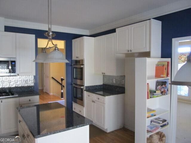 kitchen featuring backsplash, ornamental molding, stainless steel appliances, white cabinetry, and hanging light fixtures