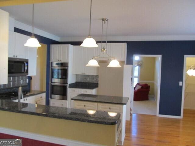 kitchen featuring white cabinetry, stainless steel appliances, light hardwood / wood-style flooring, pendant lighting, and decorative backsplash