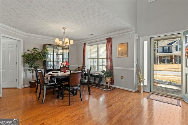 dining area with hardwood / wood-style flooring, ornamental molding, a textured ceiling, and a chandelier