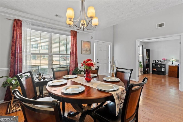 dining room featuring a textured ceiling, light hardwood / wood-style floors, crown molding, and a notable chandelier