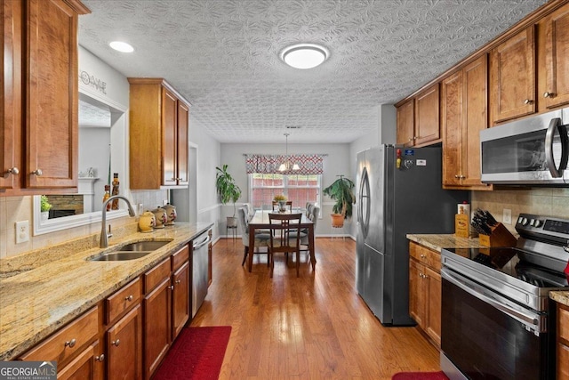 kitchen featuring sink, a textured ceiling, decorative light fixtures, appliances with stainless steel finishes, and light wood-type flooring