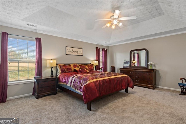 carpeted bedroom featuring ceiling fan, a textured ceiling, a tray ceiling, and multiple windows