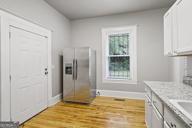 kitchen featuring light stone countertops, stainless steel refrigerator with ice dispenser, sink, light hardwood / wood-style flooring, and white cabinetry