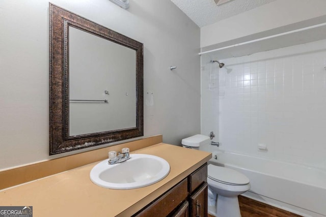 full bathroom with hardwood / wood-style floors, vanity, tiled shower / bath, toilet, and a textured ceiling