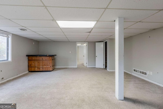 basement with a paneled ceiling and light colored carpet