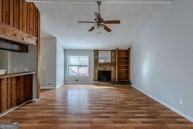 unfurnished living room with ceiling fan, a fireplace, dark wood-type flooring, and a textured ceiling