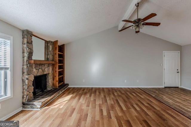 unfurnished living room featuring a textured ceiling, ceiling fan, lofted ceiling with beams, hardwood / wood-style floors, and a stone fireplace