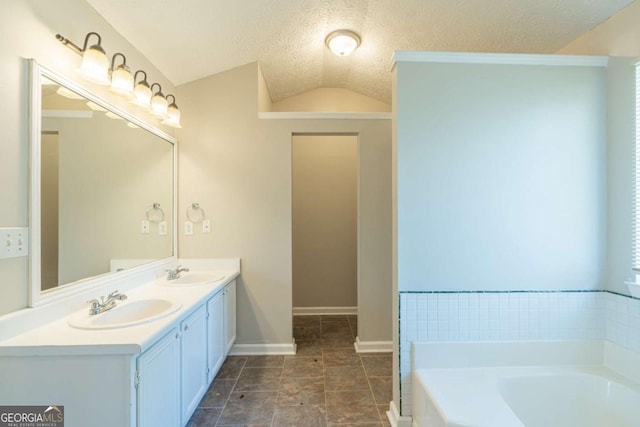 bathroom with a textured ceiling, vanity, a tub to relax in, and vaulted ceiling