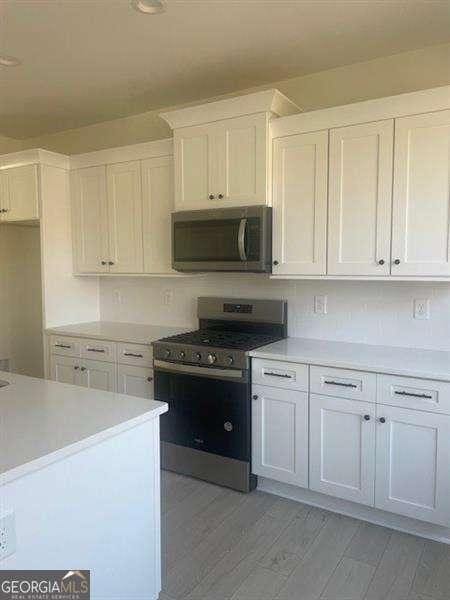 kitchen with appliances with stainless steel finishes, light hardwood / wood-style floors, and white cabinetry