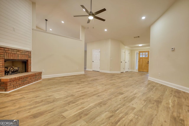 unfurnished living room with ceiling fan, high vaulted ceiling, light wood-type flooring, and a brick fireplace