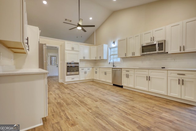 kitchen with stainless steel appliances, sink, high vaulted ceiling, light hardwood / wood-style floors, and white cabinetry