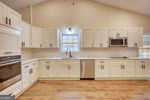 kitchen featuring backsplash, high vaulted ceiling, sink, appliances with stainless steel finishes, and light hardwood / wood-style floors