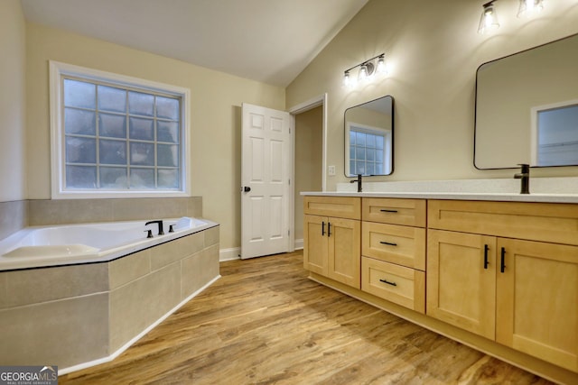 bathroom featuring hardwood / wood-style floors, vanity, vaulted ceiling, and tiled tub